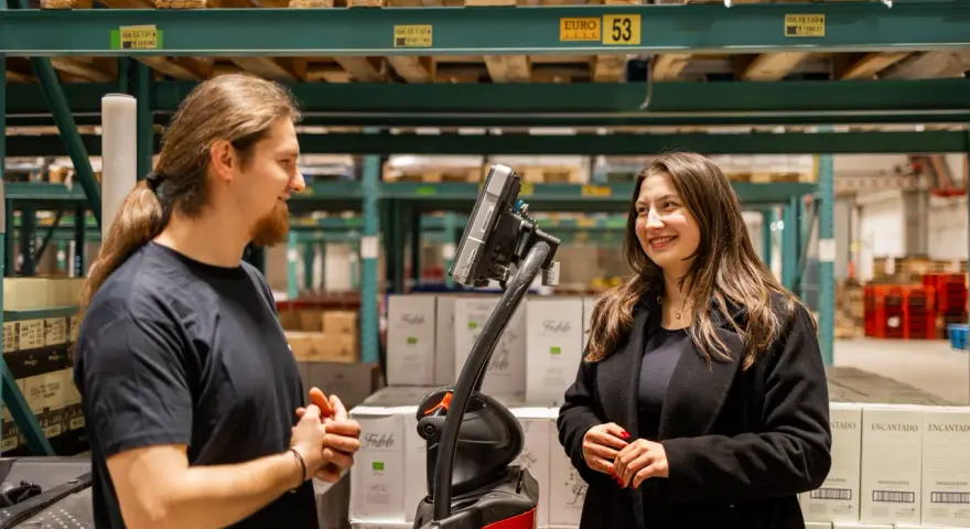 Pracownicy easywork uitzendbureau rozmawiają w magazynie, otoczeni paletami z produktami.