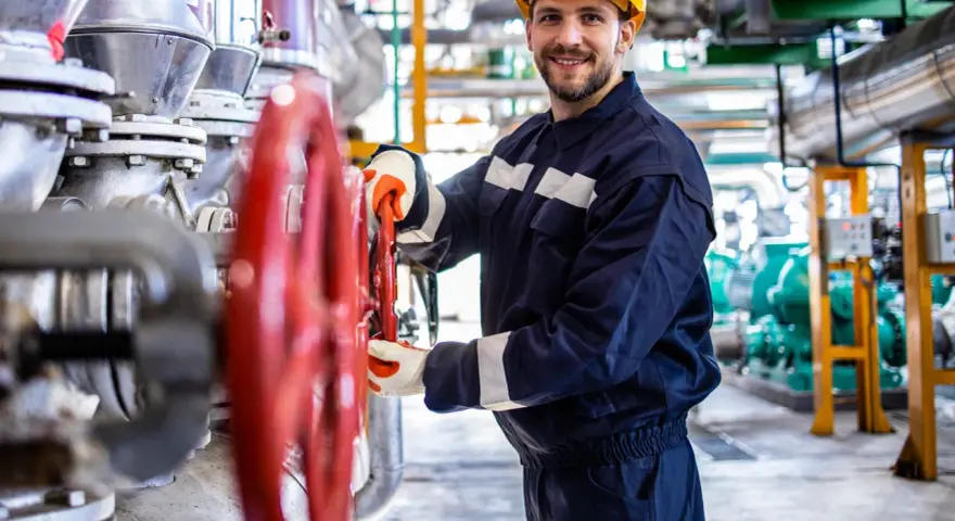 Vrolijke operator koparki holandia, met gele helm, draait aan rode kraan in industriële omgeving.