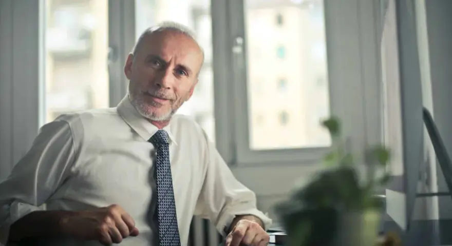 Starszy mężczyzna w białej koszuli i krawacie siedzi przy biurku. Zastanawia się, jak sprawdzić składki emerytalne w Holandii.