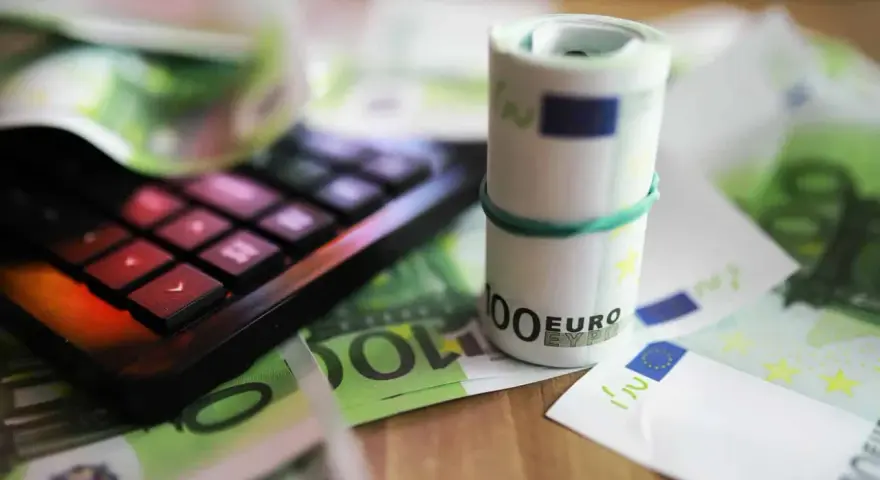 Kalkulator i zwinięte banknoty euro na tle dokumentów. Pomoc w zrozumieniu, jak wypełnić zaświadczenie o dochodach Holandia.