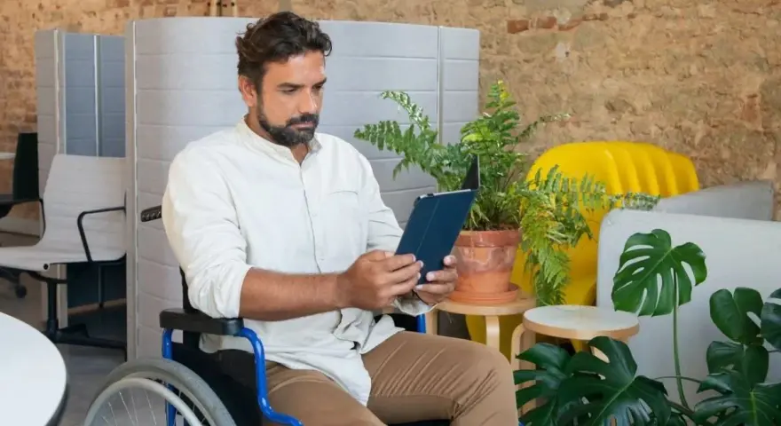 Mężczyzna na wózku inwalidzkim przegląda tablet, szukając informacji o rencie chorobowej w Holandii.