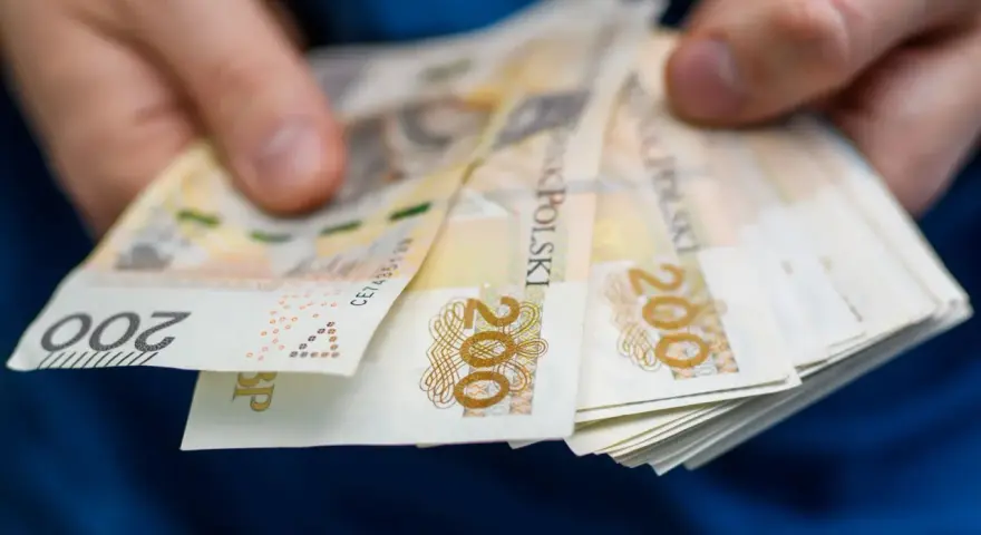 Dłonie trzymają stos banknotów 200 zł. Zastanawiasz się, ile wynosi zasiłek dla bezrobotnych?