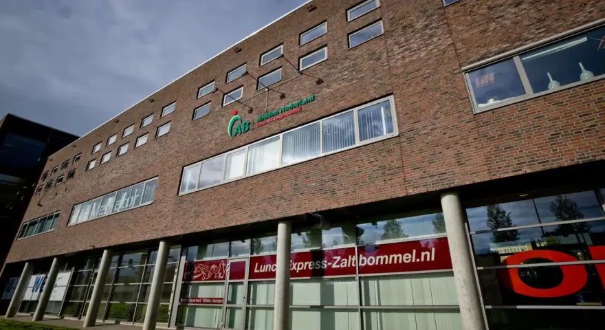Nowoczesny budynek z cegły z logo AB Midden Nederland. Na parterze szyld "Lunch express-Zaltbommel.nl".