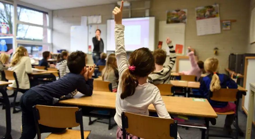Dzieci na lekcji w Holandii, z podniesionymi rękami. Dowiedz się, jak zapisać dziecko do szkoły w Holandii.