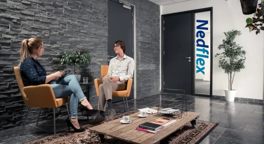 Rozmowa o pracy w Leeuwarden. Kobieta z tabletem i mężczyzna w okularach siedzą w poczekalni firmy Nedflex.