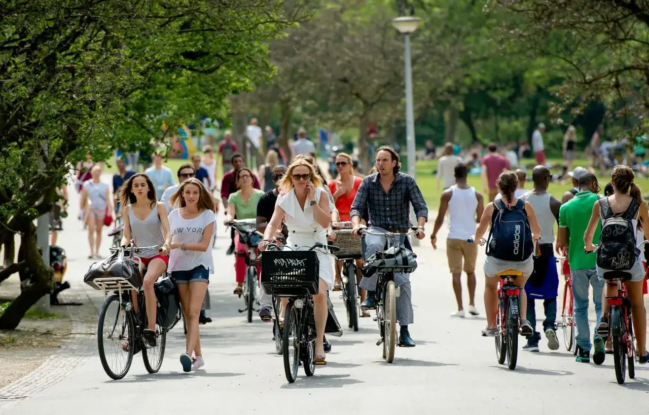 Polak w Holandii cieszy się słońcem, jadąc rowerem przez park pełen ludzi.