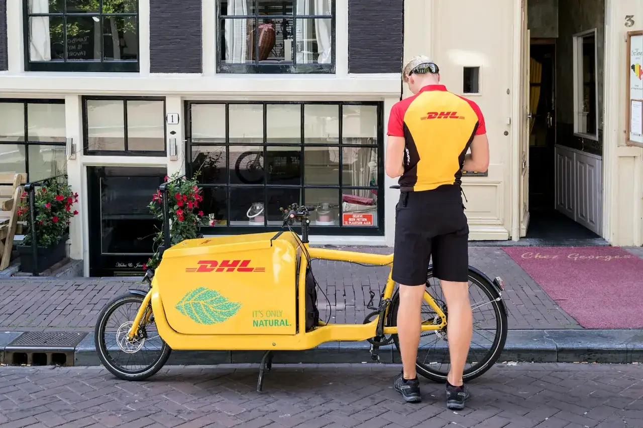 Kurier DHL z rowerem cargo na ulicy. Zastanawiasz się, ile idzie list z Polski do Holandii? Ten rower może pom&oacute;c w dostawie!