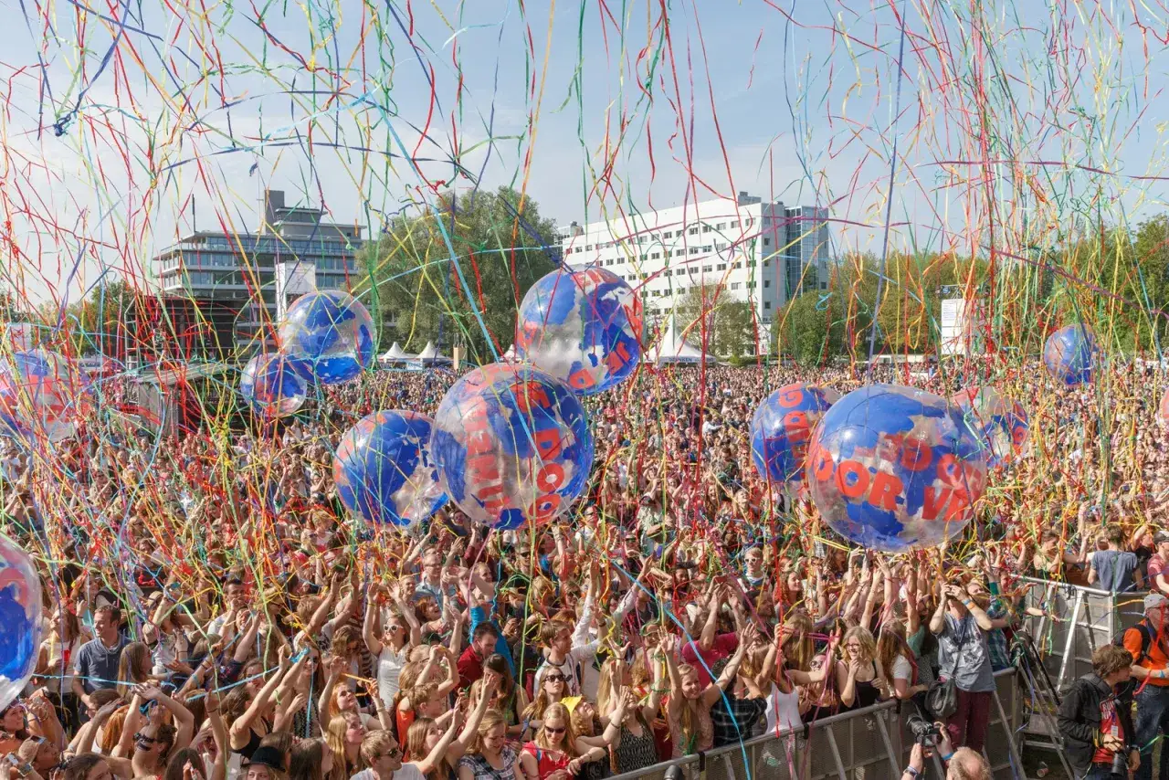 Tłumy ludzi na koncercie w Holandii, 5 maj. Kolorowe konfetti i balony unoszą się w powietrzu, tworząc radosną atmosferę.