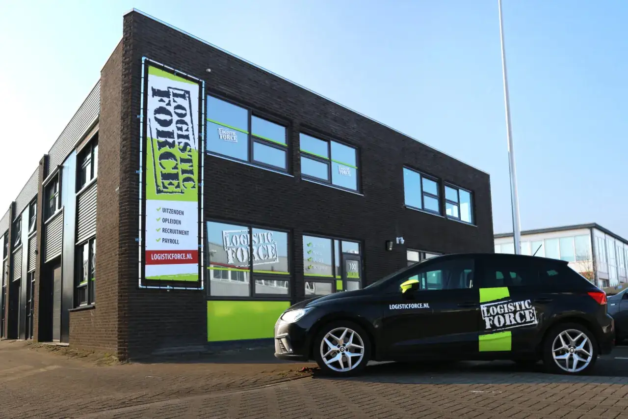 Kijk voor logistic force oferty pracy op de banner bij het gebouw. Een zwarte auto met logo staat geparkeerd.