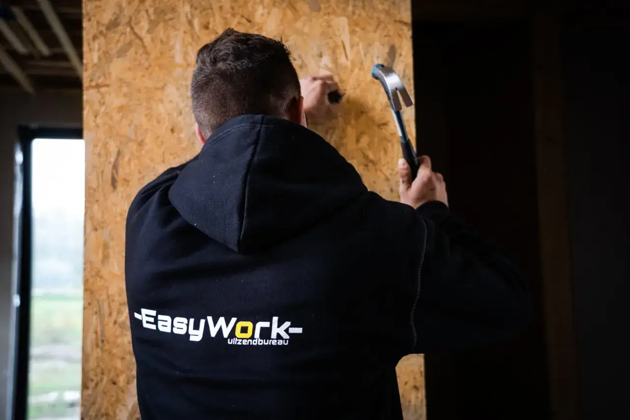 Pracownik w bluzie z logo EasyWork Lunteren wbija gwóźdź w płytę OSB.