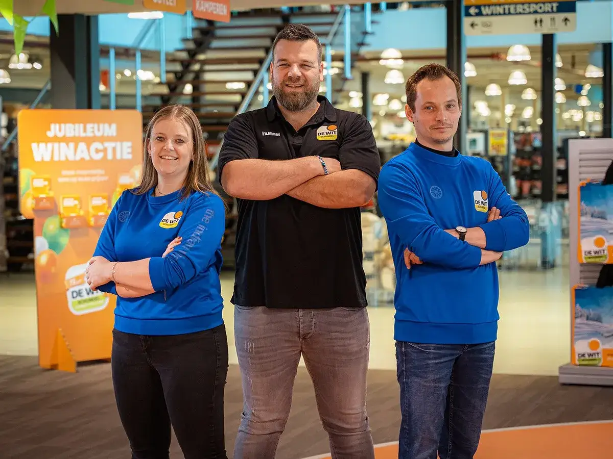 Drie medewerkers van De Wit Schijndel tonen hun synergie. Een vrouw en twee mannen, allen in bedrijfskleding, staan met gekruiste armen.