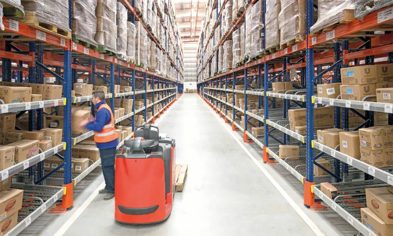 Pracownik w kamizelce odblaskowej jako order picker w Holandii pobiera paczkę z regału w magazynie.