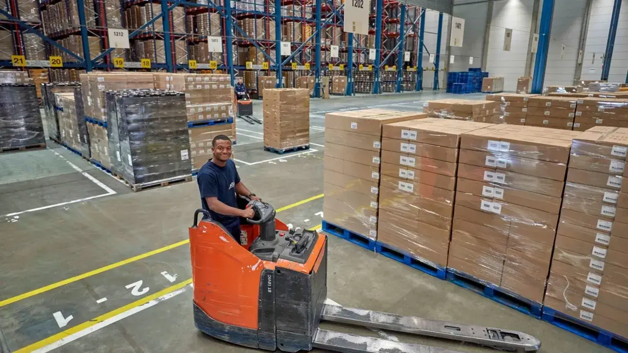 Man op een heftruck in een magazijn, omringd door dozen. Droom van praca holandia 500 euro tygodniowo? Hier wordt gewerkt!