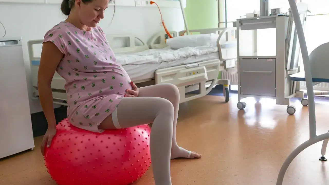 Kobieta w zaawansowanej ciąży w holandii siedzi na czerwonej piłce do ćwiczeń w szpitalnej sali.