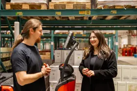 Pracownicy easywork uitzendbureau rozmawiają w magazynie, otoczeni paletami z produktami.