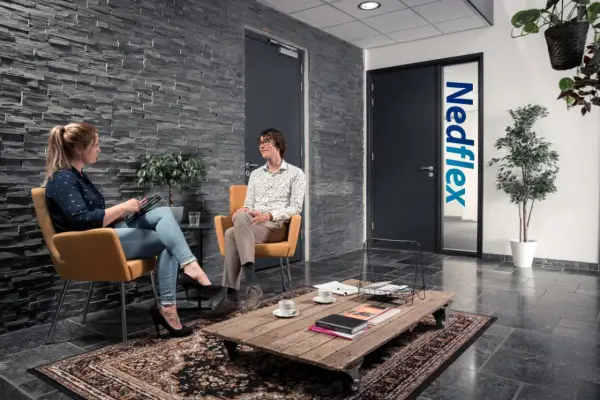 Rozmowa o pracy w Leeuwarden. Kobieta z tabletem i mężczyzna w okularach siedzą w poczekalni firmy Nedflex.